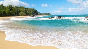Una playa con aguas turquesas cristalinas, una orilla de arena y una colina cubierta de bosque al fondo.