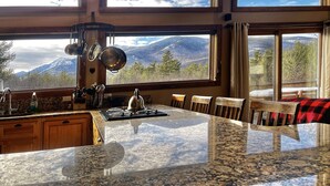 Eine Küche mit Granitarbeitsplatte, Edelstahlgeräten und Blick auf Berge durch große Fenster.