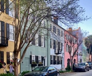 A street with colorful buildings, parked cars, and a tree.