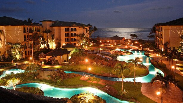 A resort with multiple swimming pools, a beach, and a view of the ocean at night.