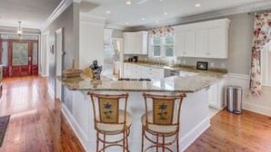A spacious kitchen with a large island, white cabinetry, and a wooden floor. - 7 41st Avenue by AvantStay | Private Pool, Near Beach (Isle of Palms)