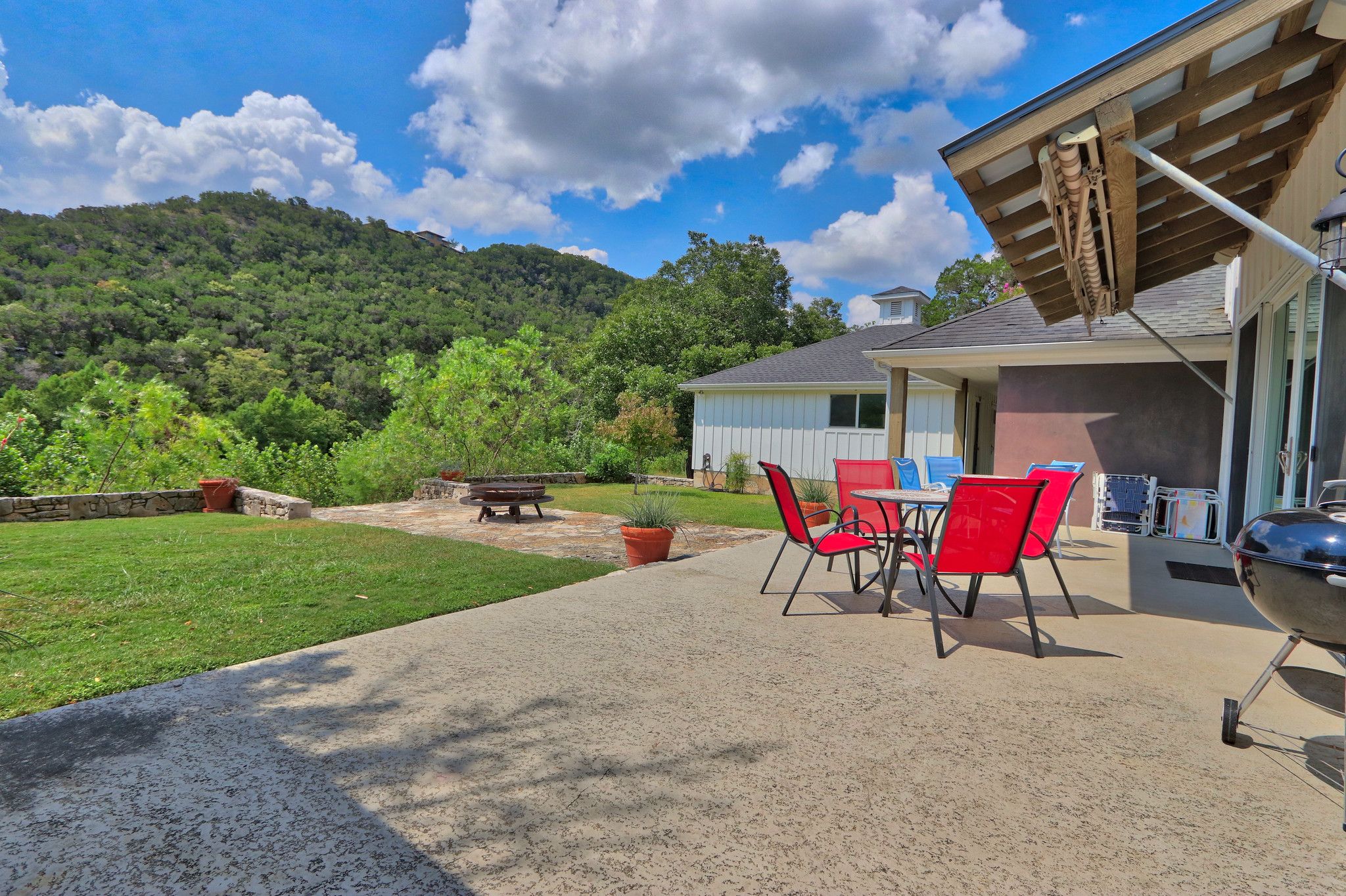 A patio with a barbecue grill, red chairs, and a table.