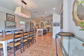 A spacious dining area with a long wooden table and multiple chairs, a kitchen in the background, and a large mirror on the right. - Relaxation awaits you. Open spaces throughout! The Blanco River welcomes you. (Wimberley)