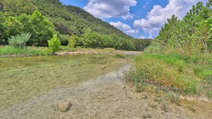Um rio límpido com pedras visíveis e vegetação nas margens.