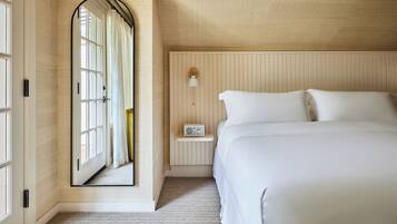 A bedroom with a large mirror, a bedside table with a radio, and a bed with white linens.