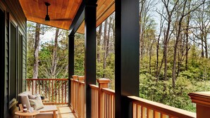 A wooden deck with a railing, a cushioned chair, and a small table with a bottle and glass. - Troutbeck (Amenia)