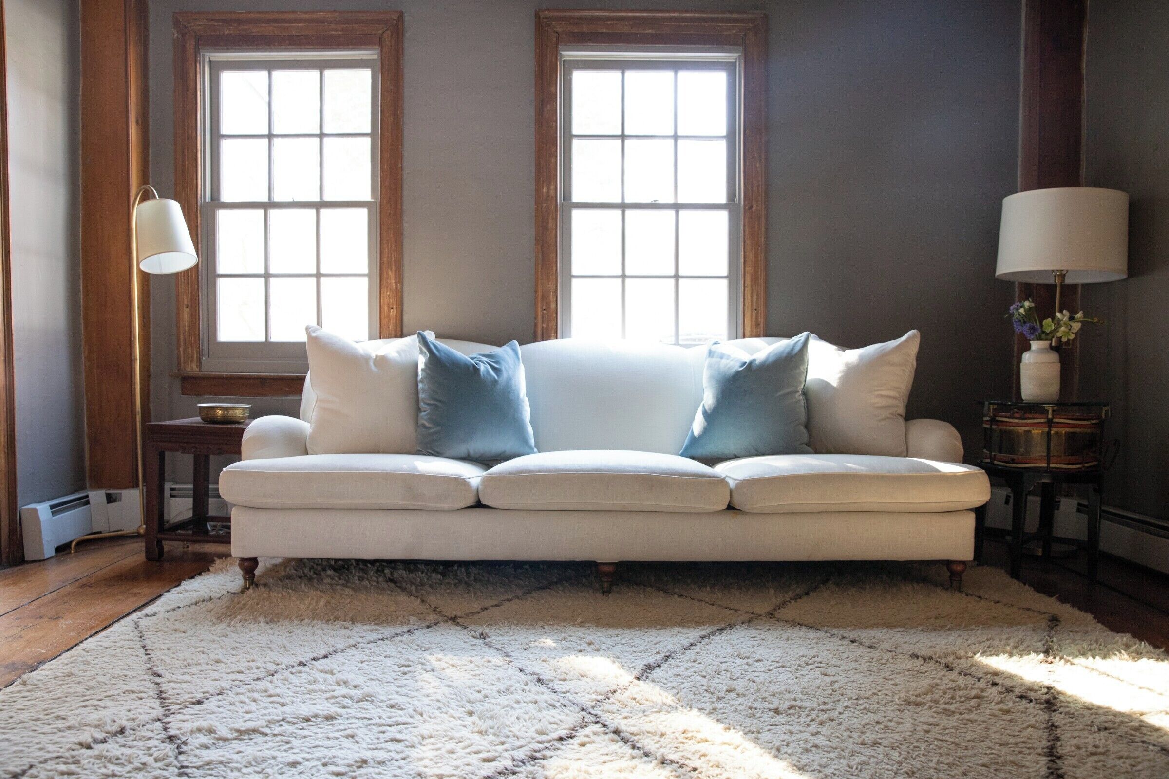 A living room with a white sofa, two windows, a lamp, and a rug.