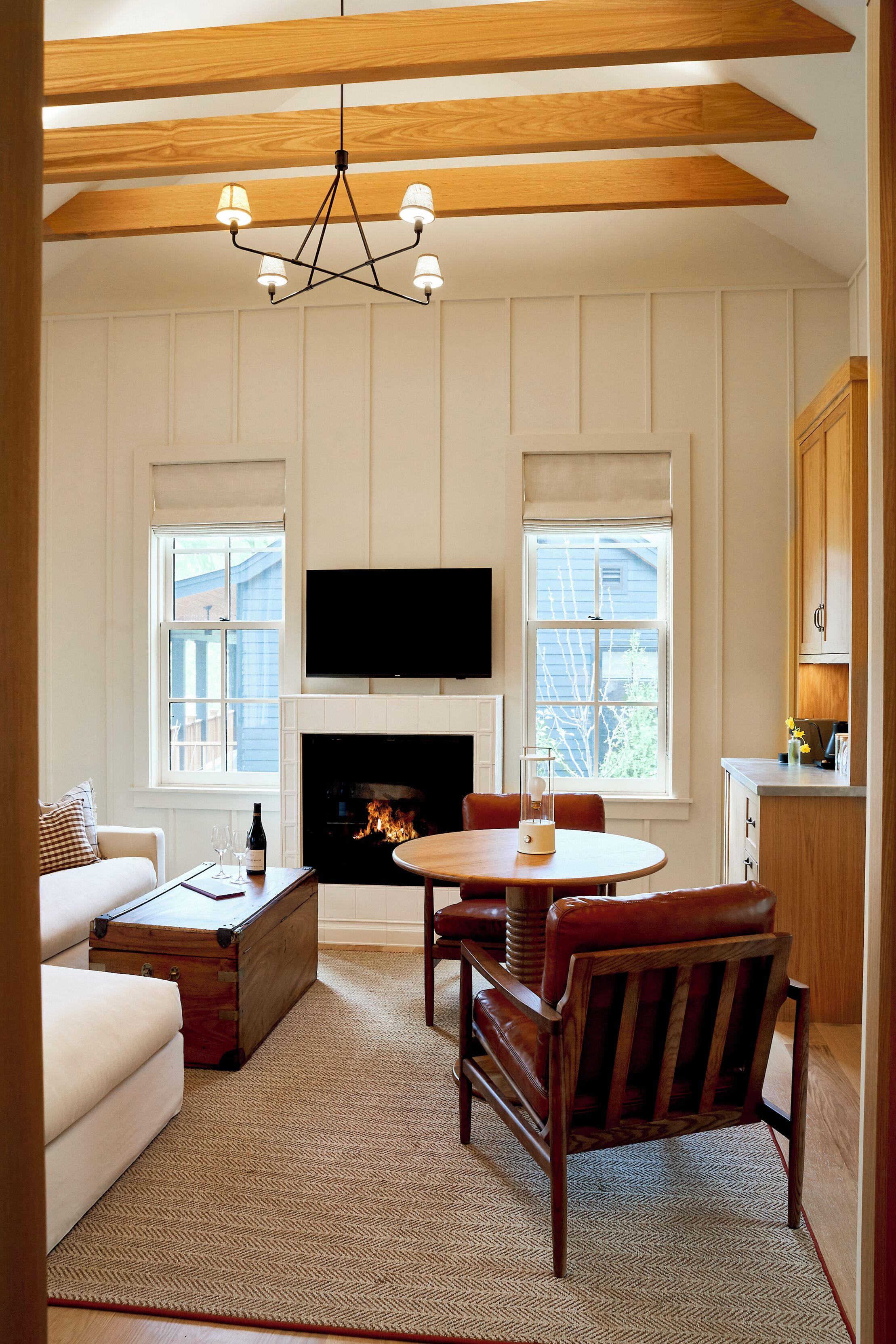 A living room with a fireplace, a television mounted above it, a dining table with chairs, and a sofa.
