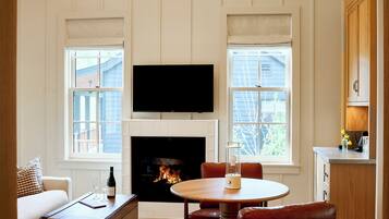 A living room with a fireplace, a television mounted above it, a dining table with chairs, and a sofa.