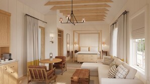 A spacious hotel room with a large bed, a sitting area with a sofa and chairs, a dining table, and a kitchen area with cabinets and a coffee machine. - Troutbeck (Amenia)