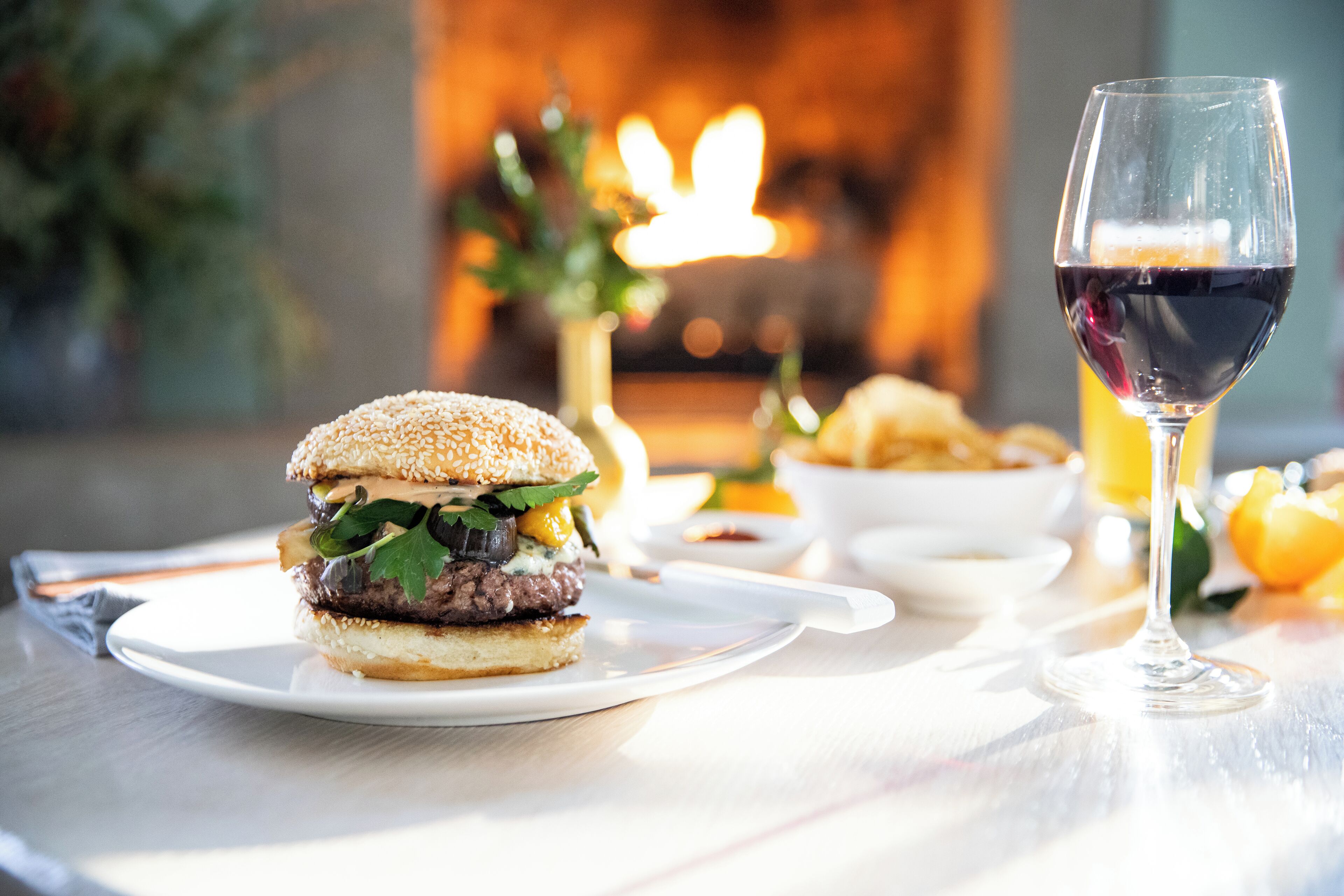 Ein Burger auf einem Teller, dazu ein Glas Rotwein und Pommes auf einem Tisch.