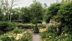 A garden pathway surrounded by various flowering plants and a wooden structure in the background. - Troutbeck (Amenia)