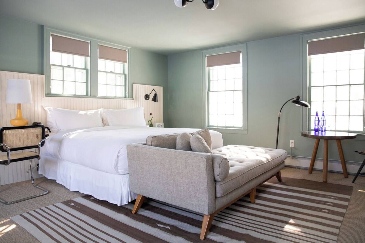 Une chambre à coucher avec un grand lit, un canapé, une lampe et une fenêtre avec des stores.