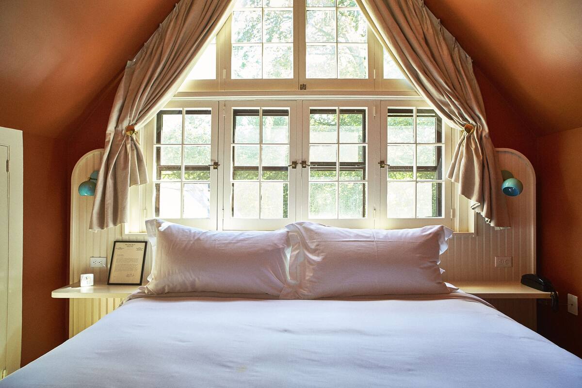 Une chambre avec un grand lit, une fenêtre avec des rideaux, une table de chevet avec une lampe et un téléphone.