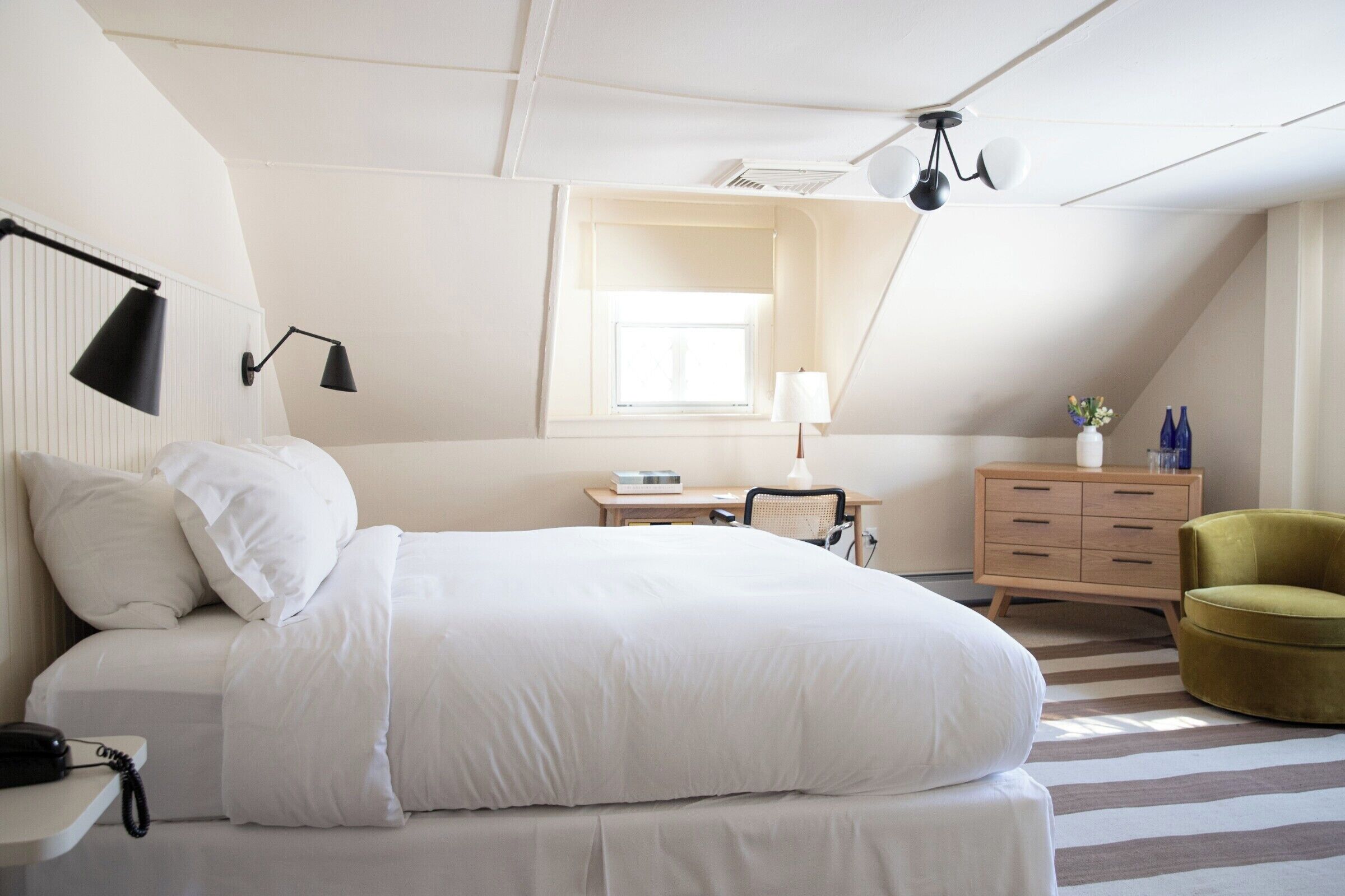 Une chambre à coucher comprenant un lit, une table de chevet, une lampe, une commode, une chaise et une fenêtre.