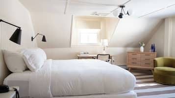 A bedroom with a bed, bedside table, lamp, dresser, chair, and a window.