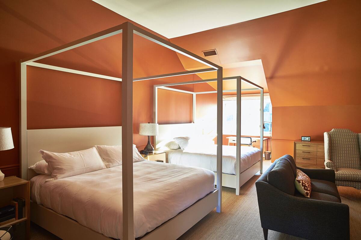 Une chambre d’hôtel avec un lit à baldaquin, un bureau avec une lampe, une chaise et une commode.