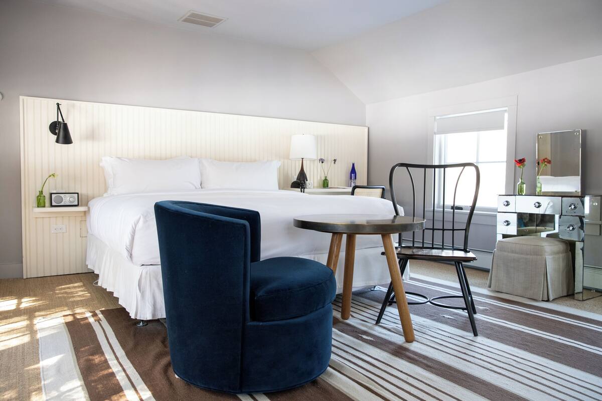 Une chambre d’hôtel avec un lit, un bureau, une chaise, une lampe et un miroir.