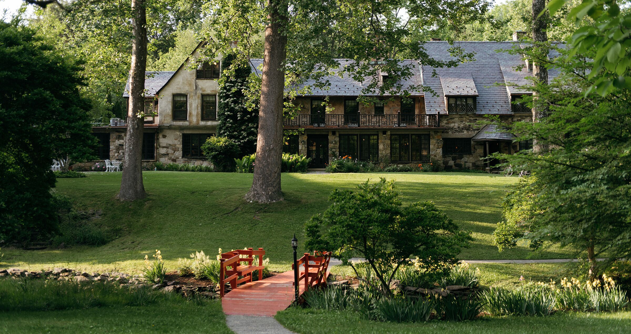A stone building with a large lawn, a red pathway, and a wooden bench.
