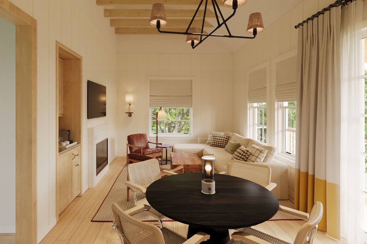 Un salon chaleureux avec une table ronde, des sièges confortables, une cheminée et une grande fenêtre agrémentée de rideaux.