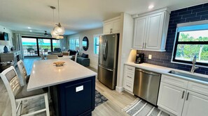 A modern kitchen with a central island, stainless steel appliances, and a view of the outdoors.