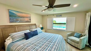 A bedroom with a bed, a ceiling fan, a window with shutters, and a chair.