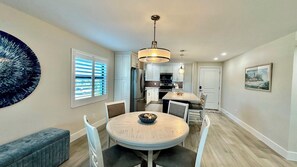 A modern kitchen with white cabinets, a central island, and a dining area with a round table and chairs.