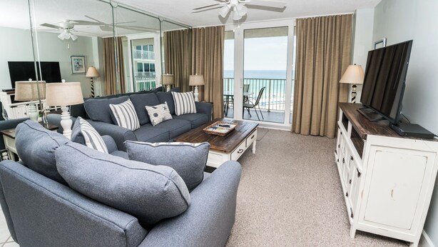 A living room with a sofa, coffee table, and TV stand. There is a balcony with curtains and a view of the ocean. - E805 Great Gulf View, 3 pools, Gym & Tennis Court (Panama City)