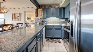 Une cuisine moderne avec des meubles de couleur bleu foncé, un réfrigérateur en acier inoxydable et un plan de travail en granit.