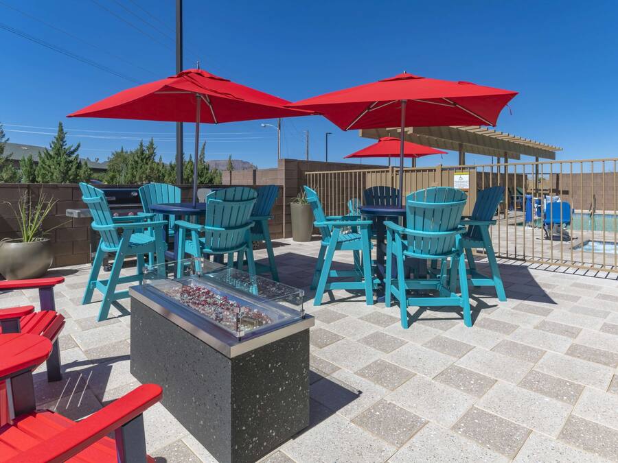 An outdoor patio with turquoise chairs and red umbrellas, a barbecue grill, and a pool area.