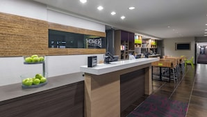 A hotel reception area with a modern design, including a reception desk, a digital screen, and a seating area with chairs and a table.
