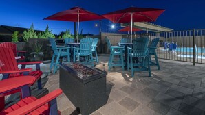 An outdoor patio with Adirondack chairs, a fire pit, and red umbrellas.