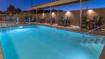 A swimming pool with chairs and umbrellas, surrounded by a brick wall and a pergola.