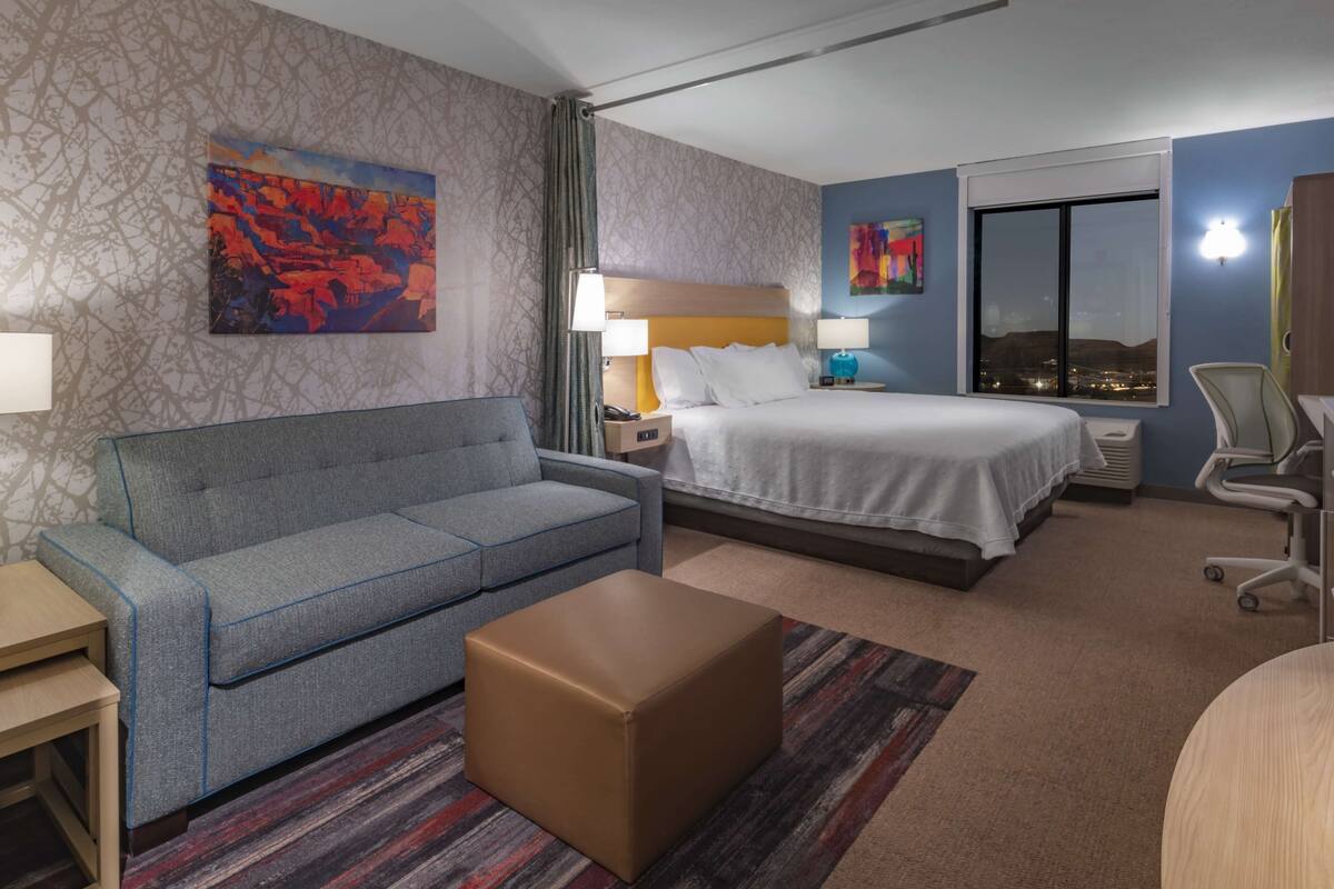 Ein Hotelzimmer mit Bett, Sofa, kleinem Tisch, Stuhl und Fenster mit Blick auf die Stadt.