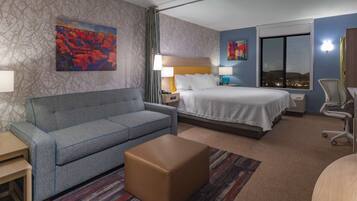 A hotel room with a bed, a sofa, a small table, a chair, and a window with a city view.