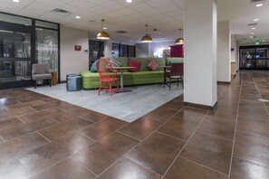 A modern lobby with a green sofa, red chairs, and a tiled floor. - Home2 Suites by Hilton Kingman (Kingman)