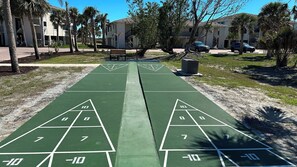 A shuffleboard court with numbered scoring areas, surrounded by palm trees and residential buildings. - Sandpiper Beach #202 ~ Reimagined. Rebuilt. Better Than Ever (Sanibel)