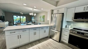A modern kitchen with white cabinetry, stainless steel appliances, and a large island. - Sandpiper Beach #202 ~ Reimagined. Rebuilt. Better Than Ever (Sanibel)