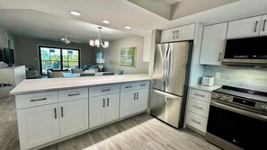 A modern kitchen with white cabinetry, stainless steel appliances, and a large island. - Sandpiper Beach #202 ~ Reimagined. Rebuilt. Better Than Ever (Sanibel)