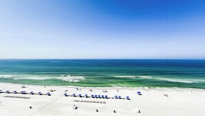 A beach with white sand, clear blue water, and a row of blue umbrellas. - D1003 Private covered parking spot, Gulf Front! (Panama City Beach)