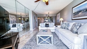 A modern living room with a white sofa, a coffee table, and a glass wall. - D1003 Private covered parking spot, Gulf Front! (Panama City Beach)