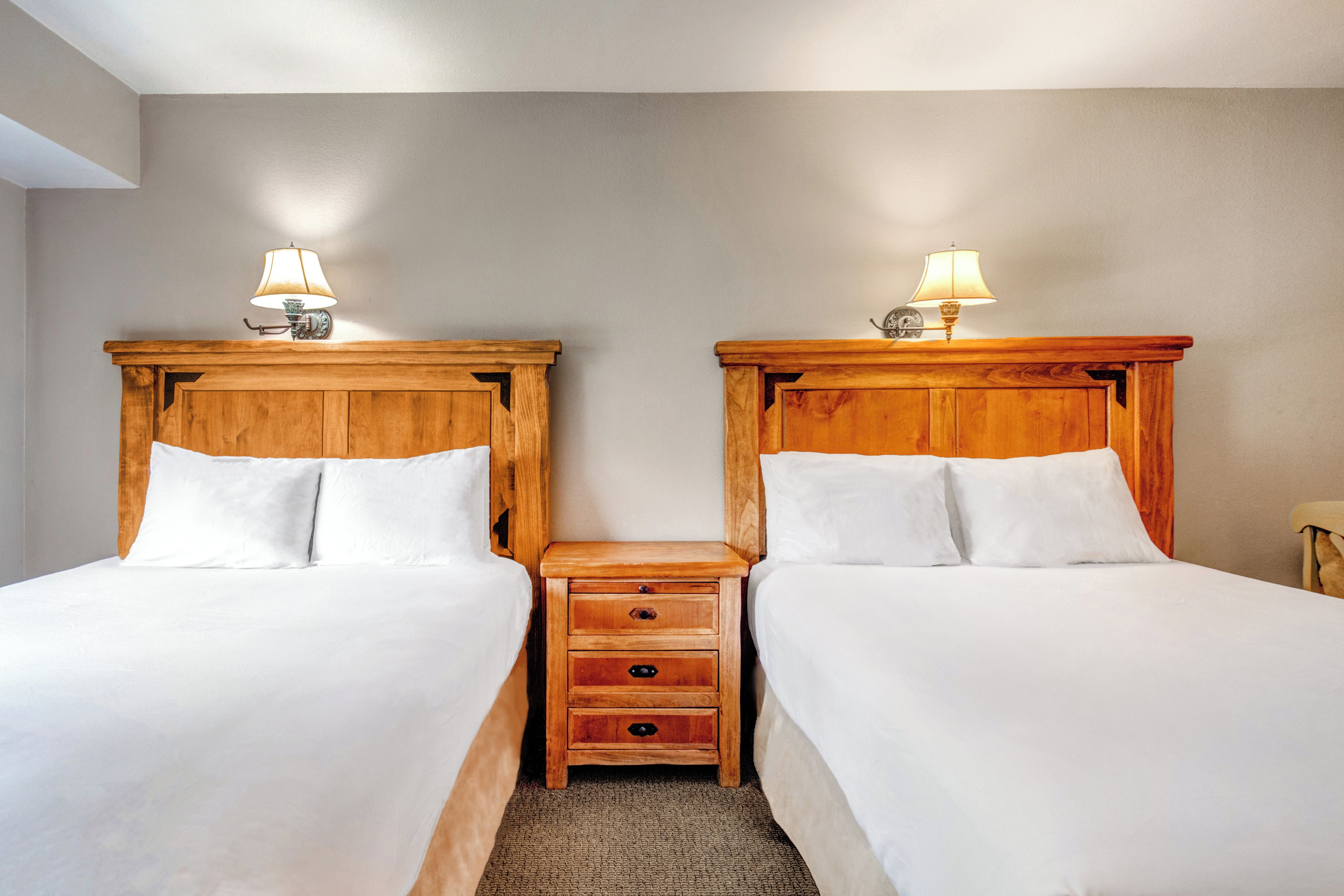 A hotel room with two wooden beds, each with a nightstand and a lamp.