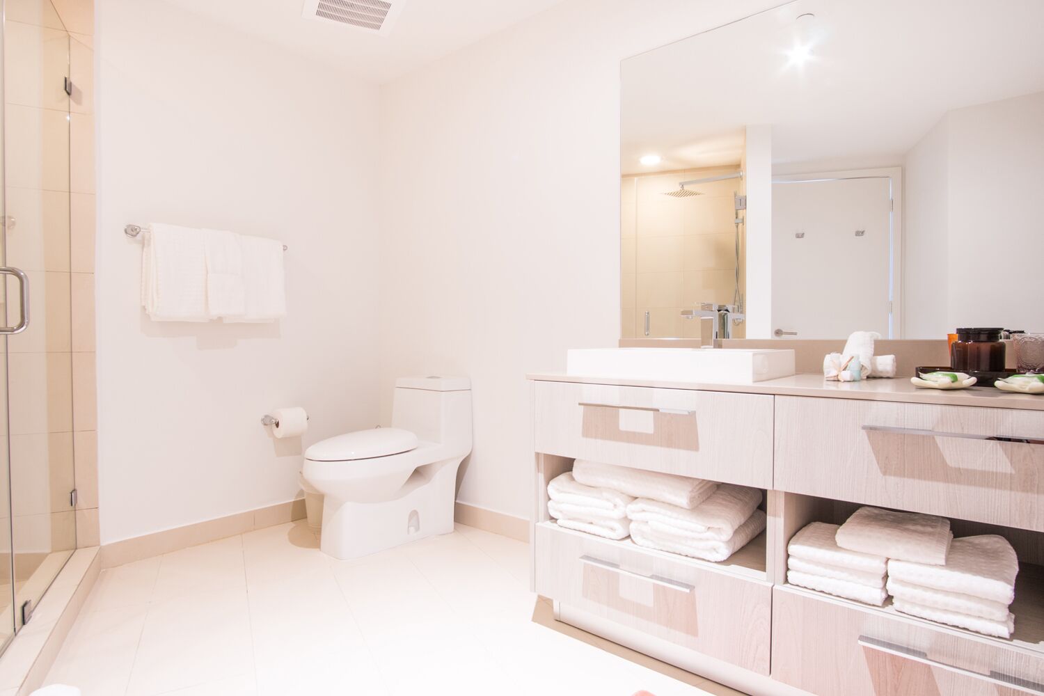 A modern bathroom with a glass shower enclosure, a white toilet, a vanity with a mirror, and neatly folded towels.