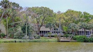 Um imóvel à beira do lago com um cais, área de estar coberta ao ar livre e uma casa grande cercada por árvores.