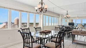 A spacious dining area with a large table and chairs, large windows with a view of the beach and cityscape, and a chandelier. - D1001 Direct Gulf-Front View, 3 Pools, Tennis (Panama City Beach)