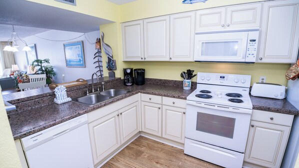 Cocina compacta con armarios blancos, horno microondas integrado, cocina y lavavajillas.