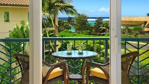 Un balcón con sillas de mimbre y una mesa, con vistas a un jardín tropical y al océano.