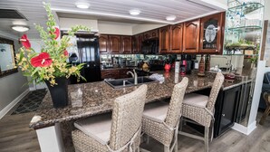A modern kitchen with granite countertops, dark wooden cabinets, and a central island with bar stools. - D601 Direct Gulf View, 3 pools, Tennis Court (Panama City)