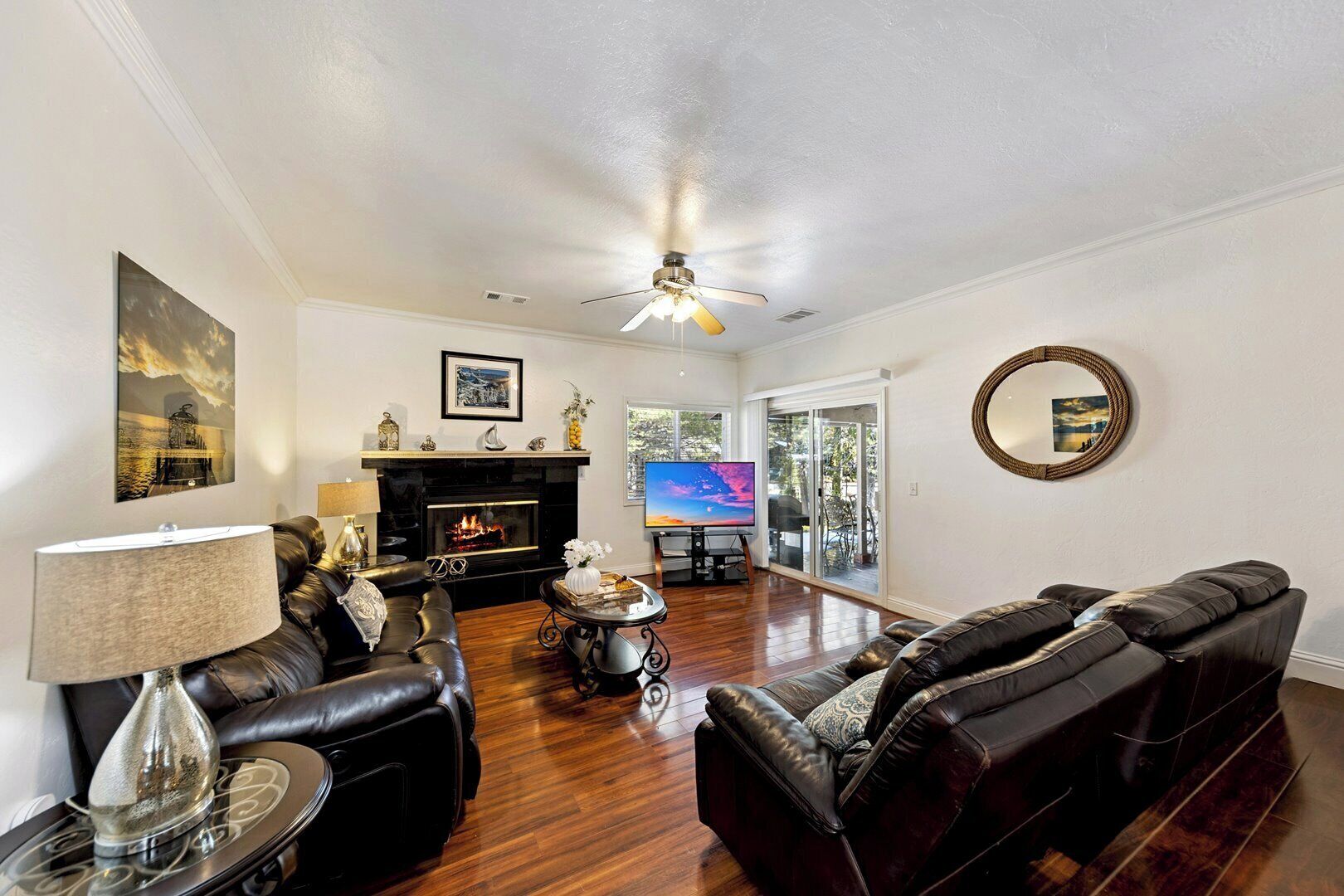 A living room with a fireplace, leather sofas, a TV, and a ceiling fan.