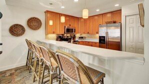 A kitchen with wooden cabinets, a microwave, a refrigerator, and a bar area with wicker chairs. - 513 Seascape by AvantStay Oceanfront Home w/ Amazing View & Community Pool (Isle of Palms)